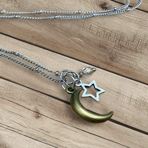 Moon and star charm necklace with crystal bead on stainless steel chain laid on wooden background