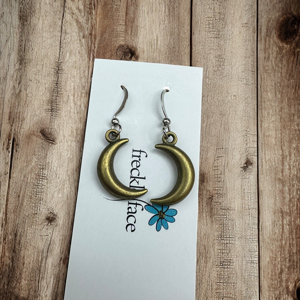Centered close-up of bronze crescent hoop earrings on a Freckle Face Jewellery card, on rustic wood.