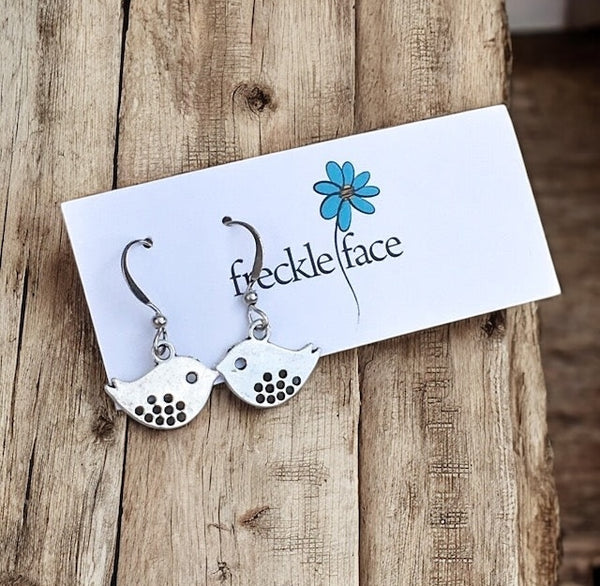 Close-up of silver plated bird cutout charm dangling from French hook with silicone stopper