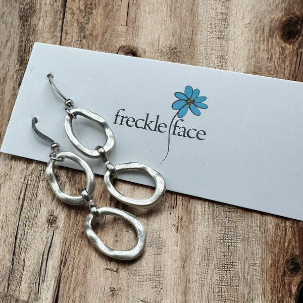 Two Matte silver dangle oval hoop earrings with wood background