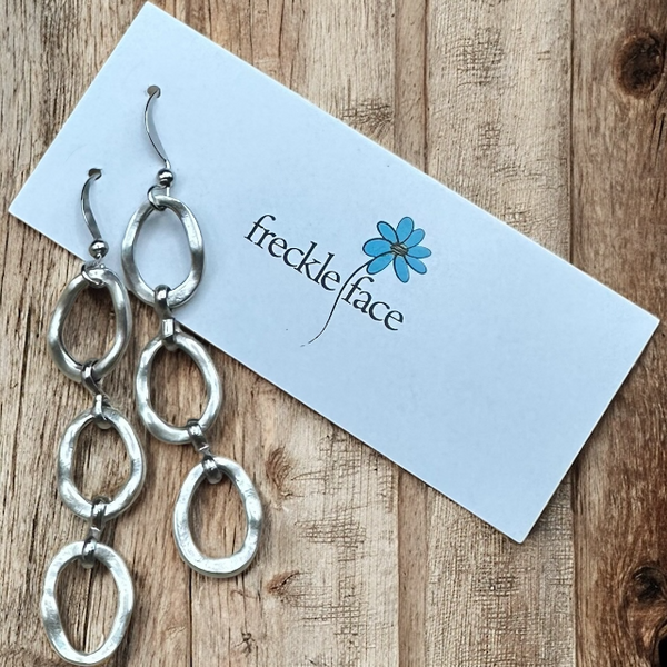 Matte silver triple oval hoop drop earrings on freckle face white earring card