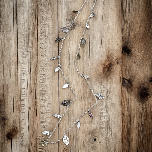 Long silver and mixed metal leaf chain necklace displayed in a soft drape on white background