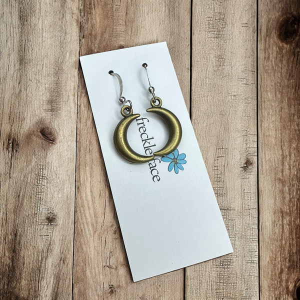 Bronze crescent hoop earrings on a Freckle Face Jewellery card, on rustic wood.