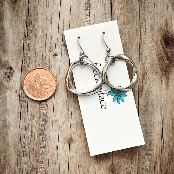 Close-up of silver-tone rhodium plated twisted hoop earrings on white background