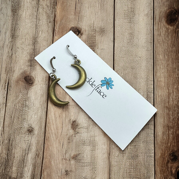 Antique bronze crescent moon earrings on branded earring card, placed on natural wood background.