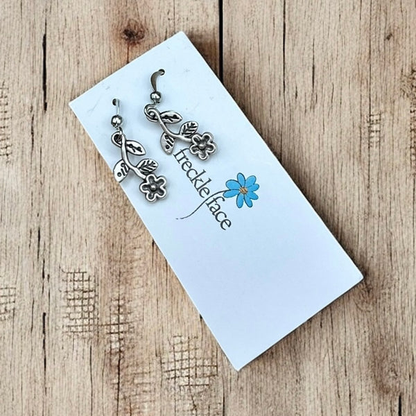 Close-up of antique silver wildflower vine earrings displayed on branded Freckle Face earring card on wood background.