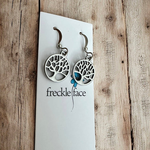 Tree silhouette dangle earrings in matte silver displayed on white card