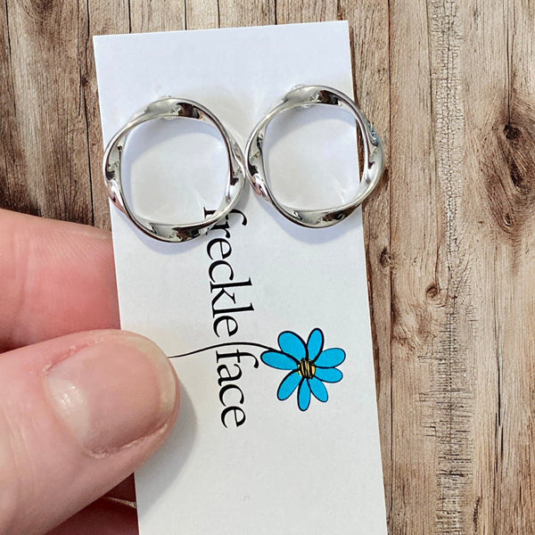 Twisted circle silver stud earrings displayed flat on neutral background