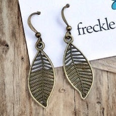 Close up of antique brass lightweight leaf earrings on wood background
