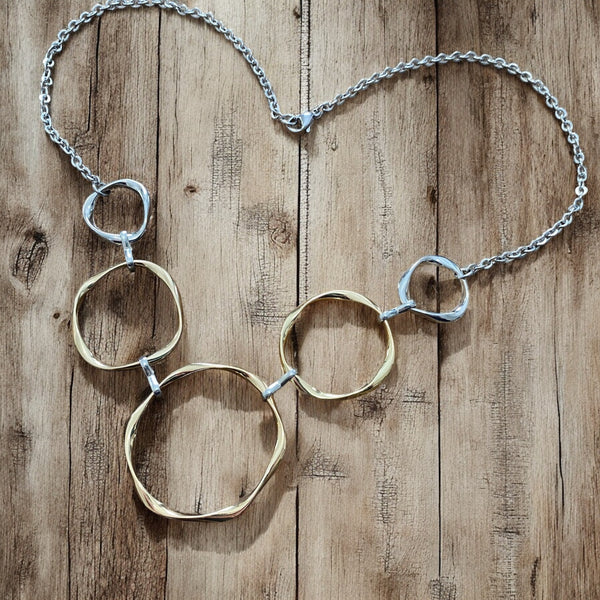 Five-ring mixed metal necklace with large central circle, two-tone design on wood surface.