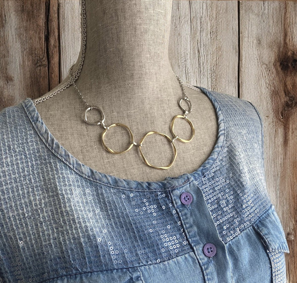 Gold and silver circle necklace displayed on mannequin in blue top, showing side view and neckline fit.
