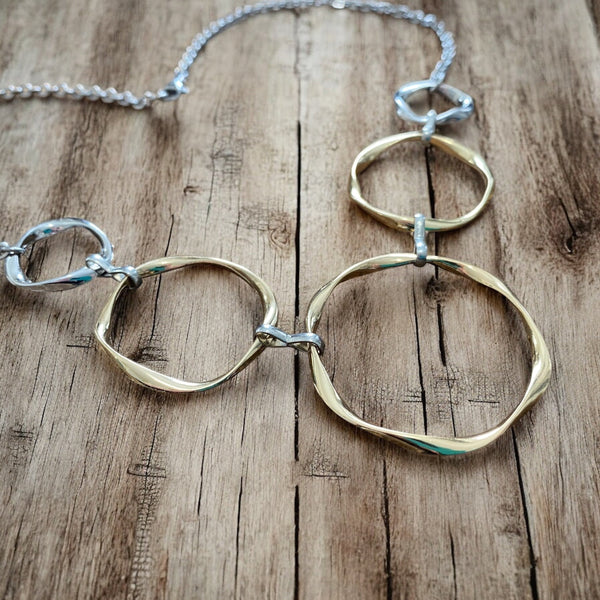 Close-up of gold and silver linked circle necklace on wood background, showing wavy ring texture and metallic shine