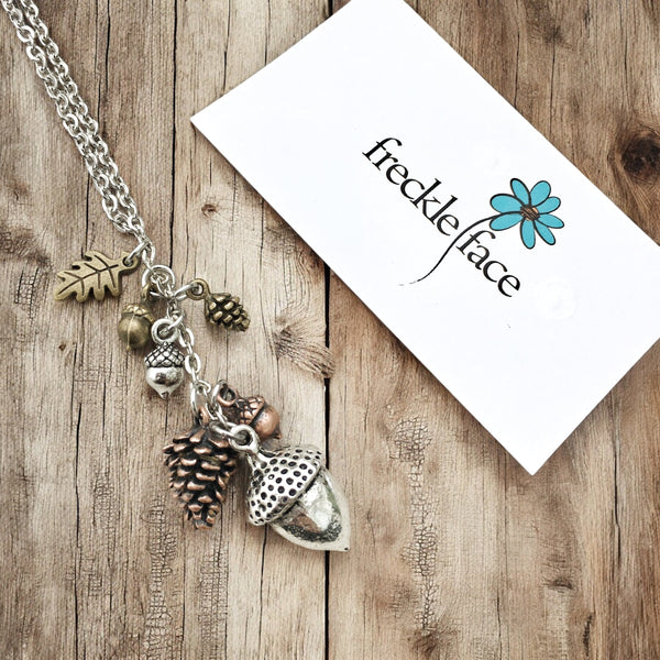 Forest charm necklace with mixed metal woodland charms beside Freckle Face Jewellery brand card.