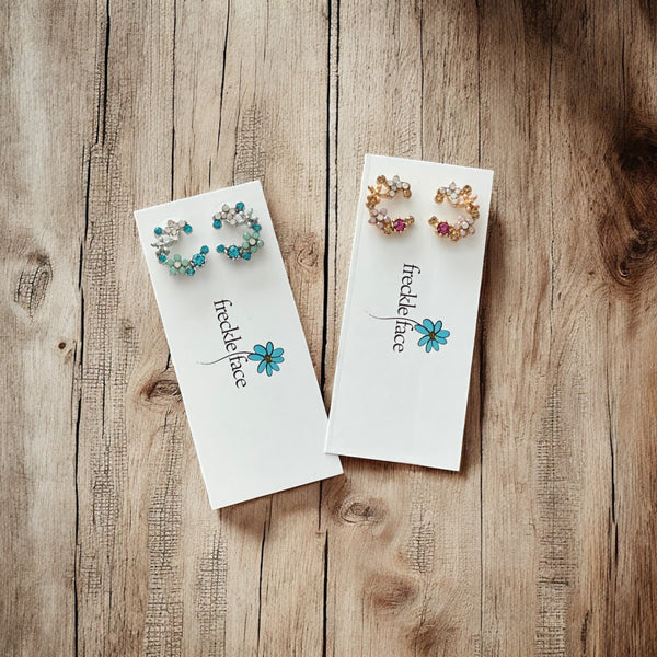 Minimalist floral crescent earrings styled on rustic wood background