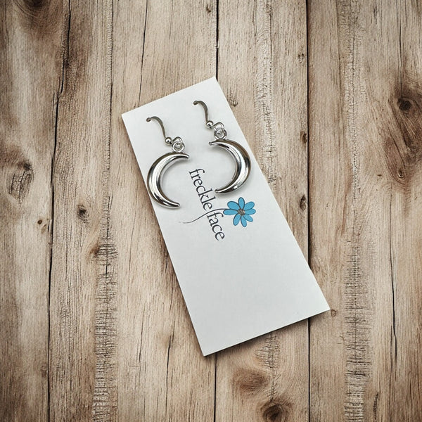 Shiny rhodium crescent moon earrings on Freckle Face Jewellery card, styled on a wooden surface.