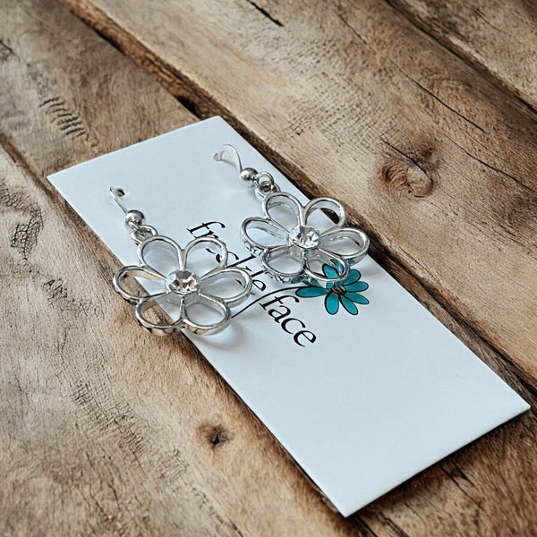 Non tarnishing rhodium plated minimalist flower earrings with tiny rhinestone in the center on wood surface