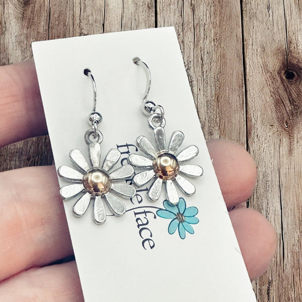 Close-up of daisy earrings with silver petals and gold center on white background