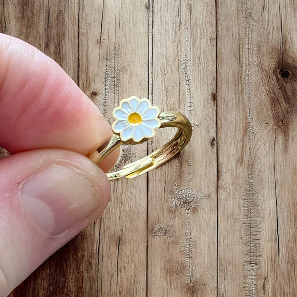gold plated ring with a white daisy design on a wooden surface.