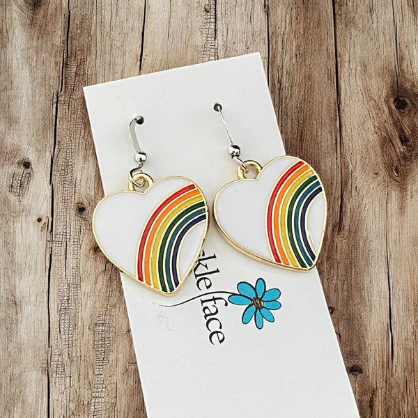 Playful rainbow heart earrings styled against rustic wood background