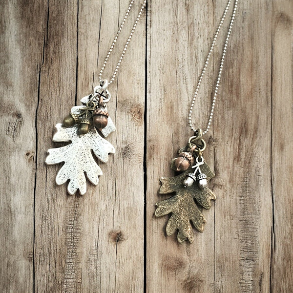 Forest-themed silver & bronze oak leaf necklace displayed on rustic wood background