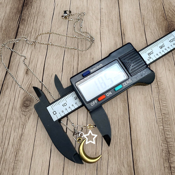 Moon and star charm necklace measured with digital caliper on wooden background