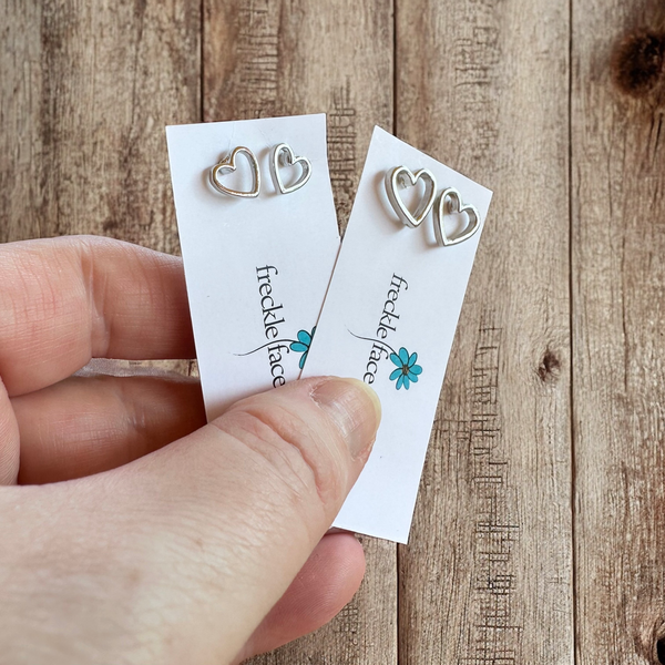 Open heart stud earring in rhodium silver, 8mm and 12 mm, displayed on freckle face jewelry brand card