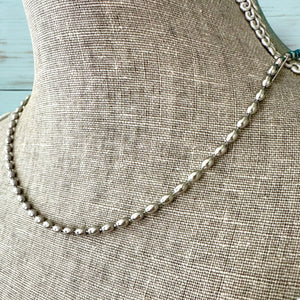 stainless steel beaded chain necklace on a mannequin bust against a textured fabric background