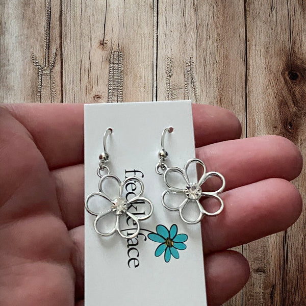 Whimsical silver flower earrings photographed on a hand with wood display
