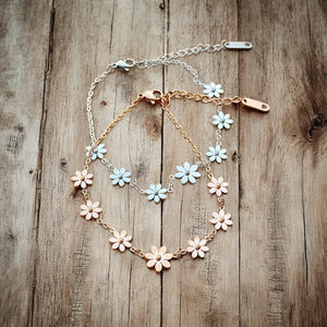 Dainty stainless steel flower anklets in rose gold and silver laid flat on wood background